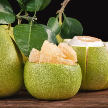 Fresh peeled pomelo, grapefruit, shaddock with green leaves on dark wooden plank table. Seasonal fruit near mid-autumn festival, close up, copy space