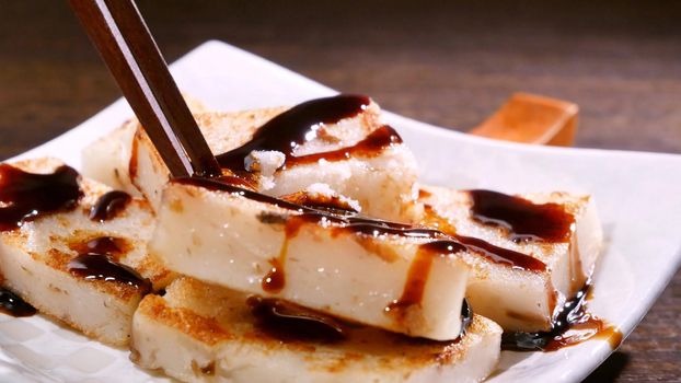 Pouring black soy sauce on ready-to-eat delicious turnip cake, Chinese traditional local dish radish cake in restaurant, close up, copy space.