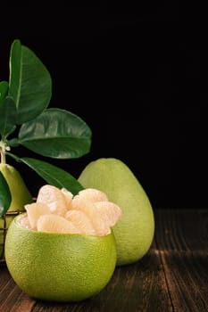 Fresh peeled pomelo, grapefruit, shaddock with green leaves on dark wooden plank table. Seasonal fruit near mid-autumn festival, close up, copy space