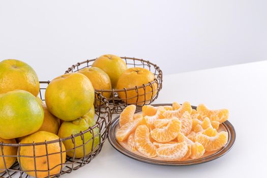 Beautiful peeled tangerines in a plate and metal basket isolated on bright white clean table in a modern contemporary kitchen island, close up.