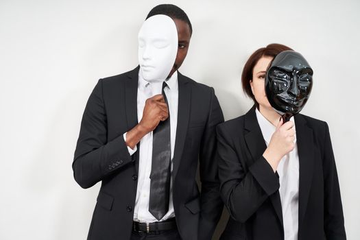African man and Caucasian woman wearing black suits hiding face with masks