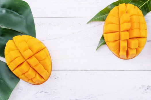 Beautiful chopped ripe mango with green leaves on bright white color wooden background, top view, flat lay, copy space. Tropical fruit design concept.
