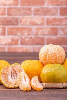 Peeled tangerines in a bamboo sieve basket on dark wooden table with red brick wall background, Chinese lunar new year fruit design concept, close up.