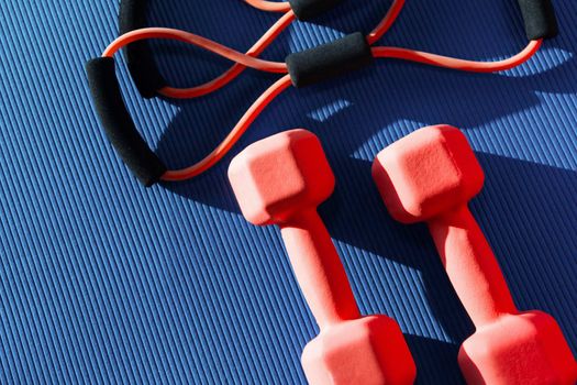 Top view of mat placed on wooden floor with bottle of water and smartphone near rubber expander in fitness club