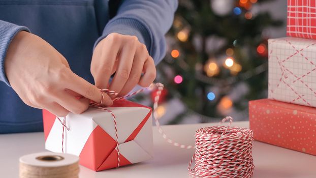 A young woman in blue is wrapping, packaging Christmas gift for kids children by beautiful, red, white wrapper with glittering light, lifestyle.