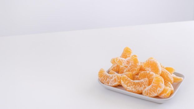 Beautiful peeled tangerines in a plate and metal basket isolated on bright white clean table in a modern contemporary kitchen island, close up.