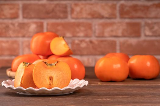 Sliced sweet persimmon kaki in a bamboo sieve basket on dark wooden table with red brick wall background, Chinese lunar new year fruit design concept, close up.
