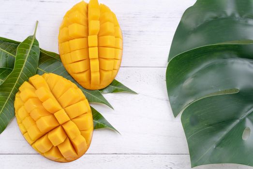 Beautiful chopped ripe mango with green leaves on bright white color wooden background, top view, flat lay, copy space. Tropical fruit design concept.