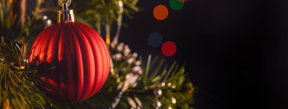 Beautiful Christmas decor concept, bauble hanging on the Christmas tree with sparkling light spot, blurry dark black background, macro detail, close up.