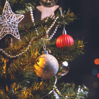 Beautiful Christmas decor concept, bauble hanging on the Christmas tree with sparkling light spot, blurry dark black background, macro detail, close up.