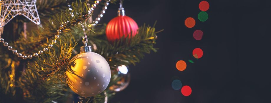 Beautiful Christmas decor concept, bauble hanging on the Christmas tree with sparkling light spot, blurry dark black background, macro detail, close up.