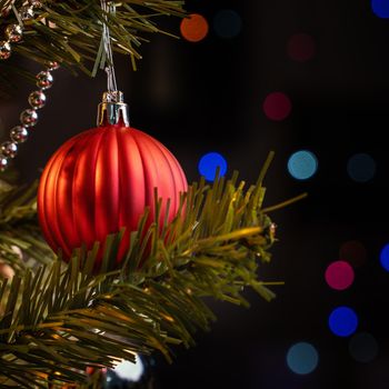 Beautiful Christmas decor concept, bauble hanging on the Christmas tree with sparkling light spot, blurry dark black background, macro detail, close up.