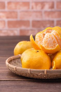 Peeled tangerines in a bamboo sieve basket on dark wooden table with red brick wall background, Chinese lunar new year fruit design concept, close up.