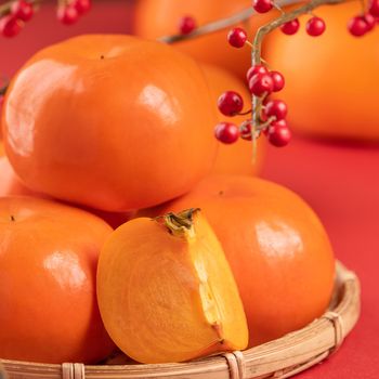 Fresh beautiful sliced sweet persimmon kaki isolated on red table background and bamboo sieve, Chinese lunar new year design concept, close up.