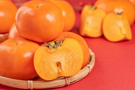Fresh beautiful sliced sweet persimmon kaki isolated on red table background and bamboo sieve, Chinese lunar new year design concept, close up.