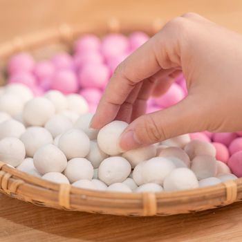 An Asia woman is making Tang yuan, yuan xiao, Chinese traditional food rice dumplings in red and white for lunar new year, winter festival, close up.