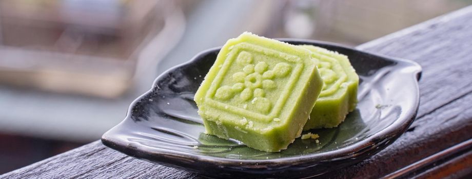 Delicious green mung bean cake with black tea plate on wooden railing of a teahouse in Taiwan with beautiful landscape in background, close up.