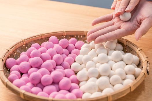 An Asia woman is making Tang yuan, yuan xiao, Chinese traditional food rice dumplings in red and white for lunar new year, winter festival, close up.