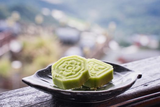 Delicious green mung bean cake with black tea plate on wooden railing of a teahouse in Taiwan with beautiful landscape in background, close up.