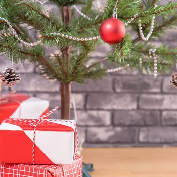 Decorated Christmas tree with wrapped beautiful red and white gifts at home with black brick wall, festive design concept, close up.