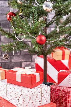 Decorated Christmas tree with wrapped beautiful red and white gifts at home with black brick wall, festive design concept, close up.