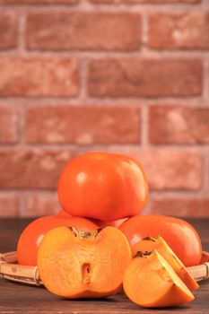 Fresh beautiful sliced sweet persimmon kaki on dark wooden table with red brick wall background, Chinese lunar new year fruit design concept, close up.