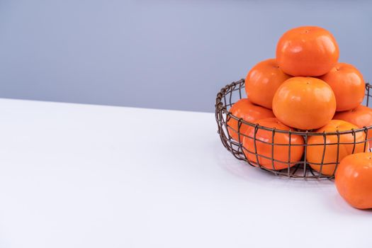 Fresh beautiful sliced sweet persimmon kaki isolated on white kitchen table with gray blue background, Chinese lunar new year design concept, close up.