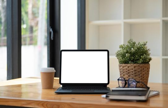 Shot of digital tablet with blank white screen, keyboard, cup of coffee on workspace desk.