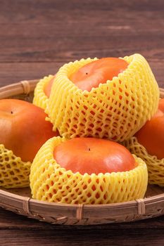 Fresh, beautiful orange color persimmon kaki on bamboo sieve over dark wooden table. Seasonal, traditional fruit of Chinese lunar new year, close up.