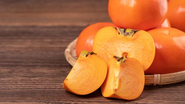 Fresh, beautiful orange color persimmon kaki on bamboo sieve over dark wooden table. Seasonal, traditional fruit of Chinese lunar new year, close up.