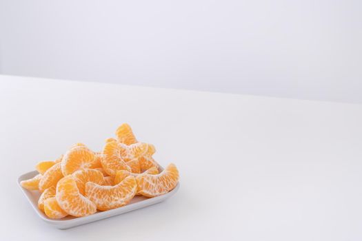 Beautiful peeled tangerines in a plate and metal basket isolated on bright white clean table in a modern contemporary kitchen island, close up.