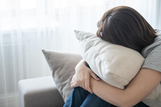 Sad depressed woman at home, she is sitting on the couch and hugging a pillow, loneliness and sadness concept