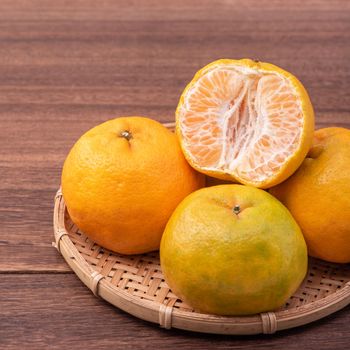 Fresh, beautiful orange color tangerine on bamboo sieve over dark wooden table. Seasonal, traditional fruit of Chinese lunar new year, close up.