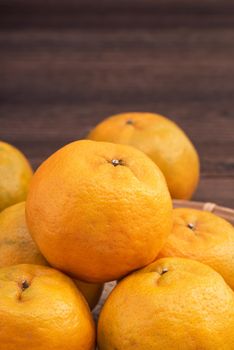 Fresh, beautiful orange color tangerine on bamboo sieve over dark wooden table. Seasonal, traditional fruit of Chinese lunar new year, close up.