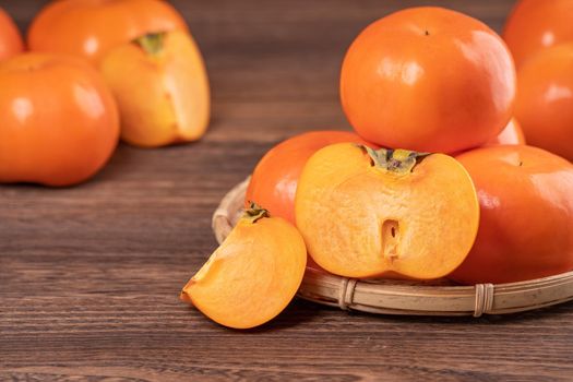 Fresh, beautiful orange color persimmon kaki on bamboo sieve over dark wooden table. Seasonal, traditional fruit of Chinese lunar new year, close up.