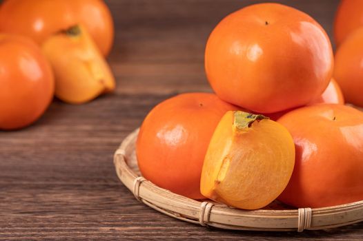 Fresh, beautiful orange color persimmon kaki on bamboo sieve over dark wooden table. Seasonal, traditional fruit of Chinese lunar new year, close up.