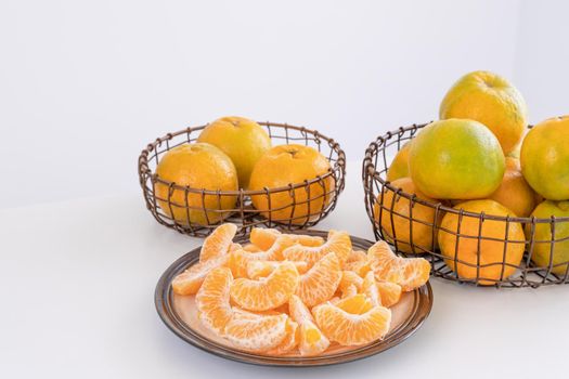 Beautiful peeled tangerines in a plate and metal basket isolated on bright white clean table in a modern contemporary kitchen island, close up.