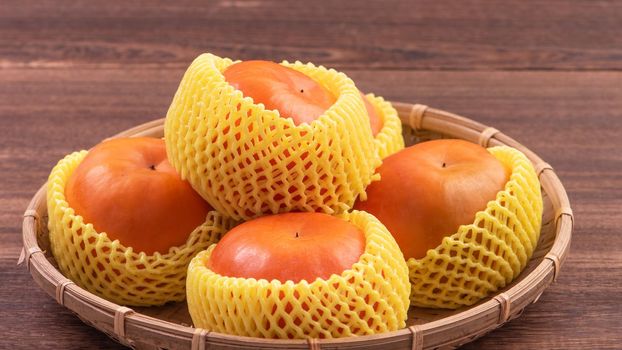 Fresh, beautiful orange color persimmon kaki on bamboo sieve over dark wooden table. Seasonal, traditional fruit of Chinese lunar new year, close up.