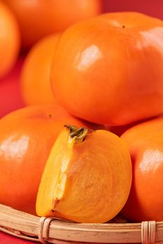 Fresh beautiful sliced sweet persimmon kaki isolated on red table background and bamboo sieve, Chinese lunar new year design concept, close up.