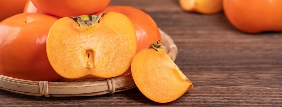 Fresh, beautiful orange color persimmon kaki on bamboo sieve over dark wooden table. Seasonal, traditional fruit of Chinese lunar new year, close up.