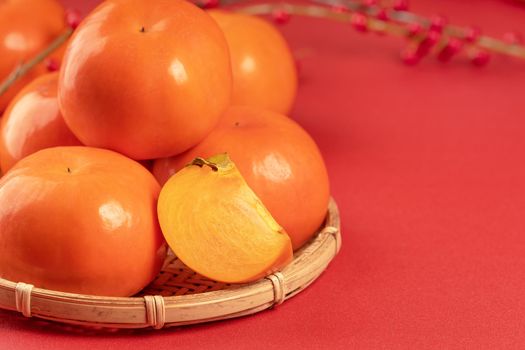 Fresh beautiful sliced sweet persimmon kaki isolated on red table background and bamboo sieve, Chinese lunar new year design concept, close up.