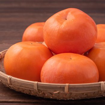 Fresh, beautiful orange color persimmon kaki on bamboo sieve over dark wooden table. Seasonal, traditional fruit of Chinese lunar new year, close up.