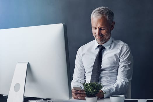 Replying to a text. a mature businessman sending a text while working on his computer