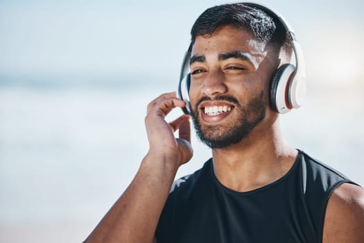 Happy, beach and a man with music for fitness, running motivation and ideas in nature. Smile, wellness and an athlete listening or streaming a podcast while training or exercise vision at the sea.