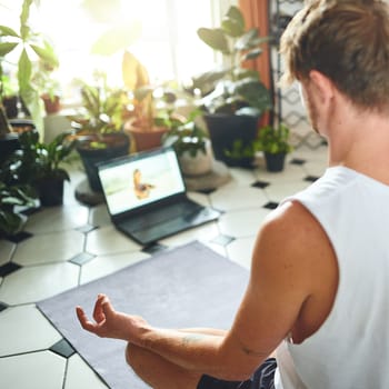 Yoga class brought straight to you. a young man using a laptop while meditating in the lotus position at home