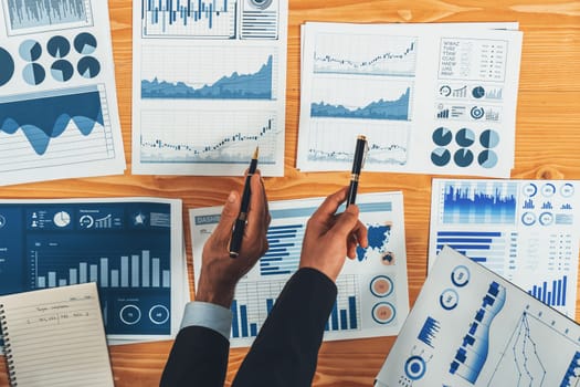 Top view analyst team discussing financial data on digital dashboard, analyzing chart and graph papers by data science software on wooden table background. Business intelligence and Fintech. Fervent