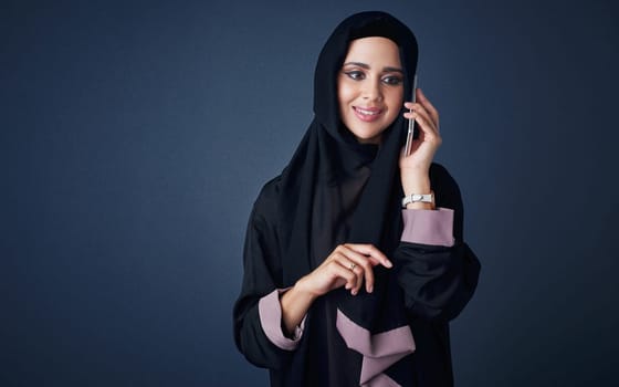 Stay in contact, stay happy. Studio shot of a young woman wearing a burqa and using a mobile phone against a gray background