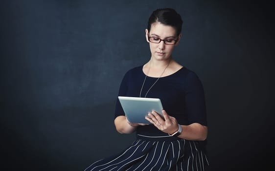 Reading up on the latest in corporate trends. Studio portrait of a corporate businesswoman using a digital tablet against a dark background
