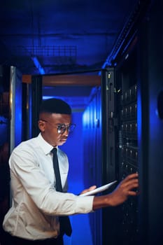 This system is in dire need of an upgrade. a young man using a digital tablet while working in a server room