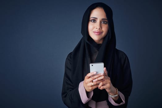 Im connected, lets chat. Studio portrait of a young woman wearing a burqa and using a mobile phone against a gray background
